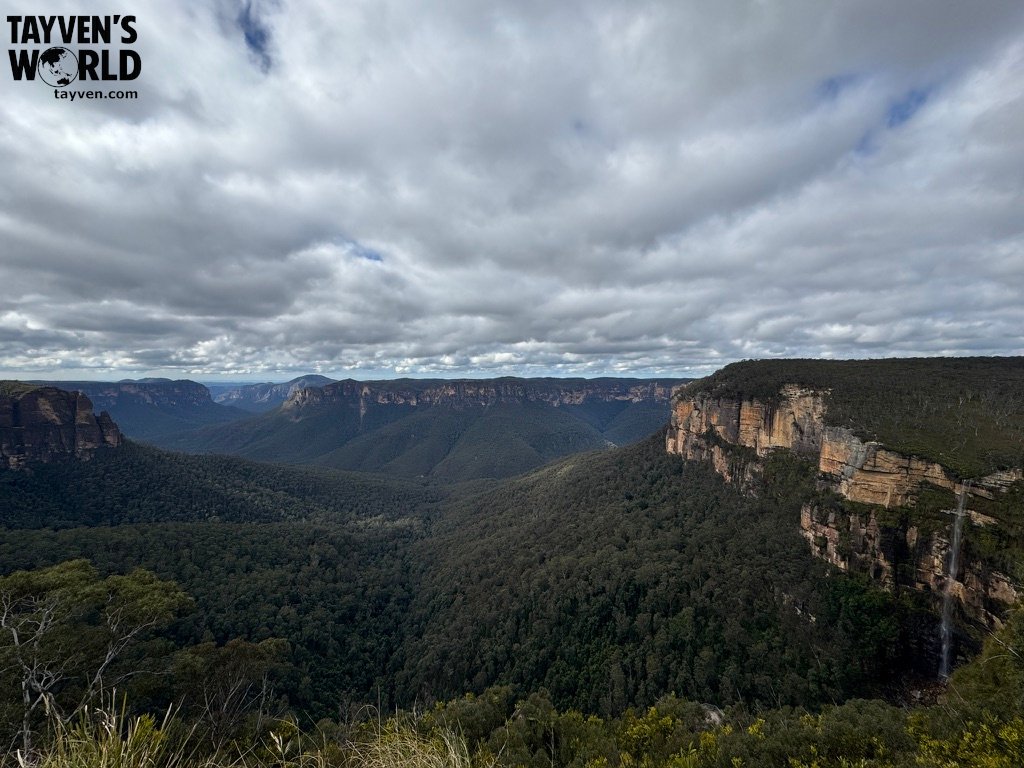 Wide view of Grose Valley with cliffs, forest, and waterfall under cloudy skies.