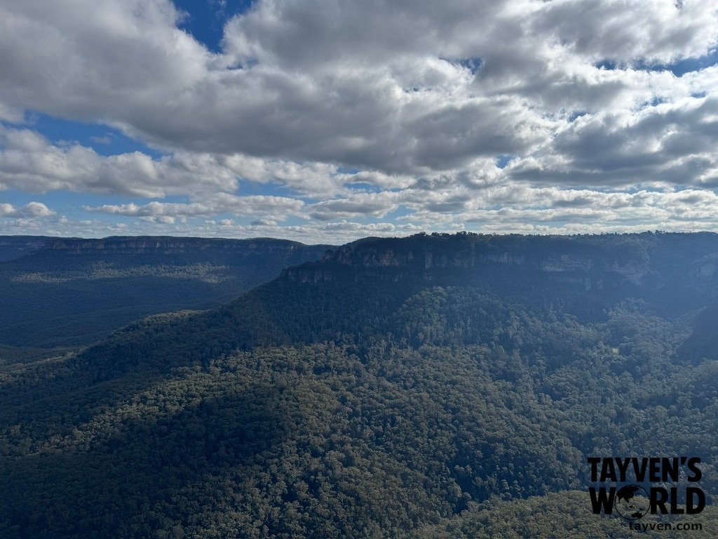 View from Sublime Point lookout showing sandstone cliffs, deep valley forest, and distant mountain ridges in the Blue Mountains.
