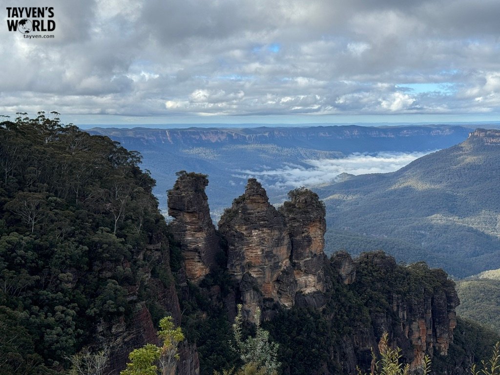 The Three Sisters rock formation rising above forested valley in the Blue Mountains.