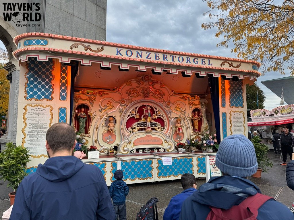 Ornate fairground concert organ labeled “Konzertorgel” with carved figures and pastel decorations.
