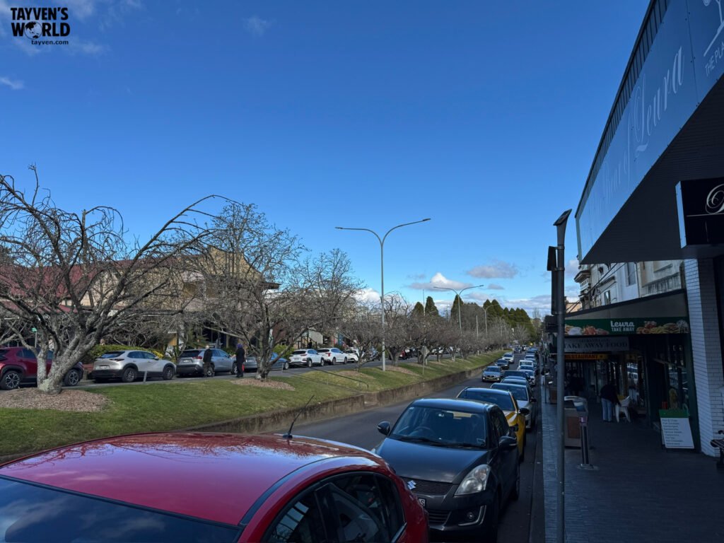 Busy Leura main street lined with parked cars, leafless trees, and local shops under a clear blue sky in the Blue Mountains.