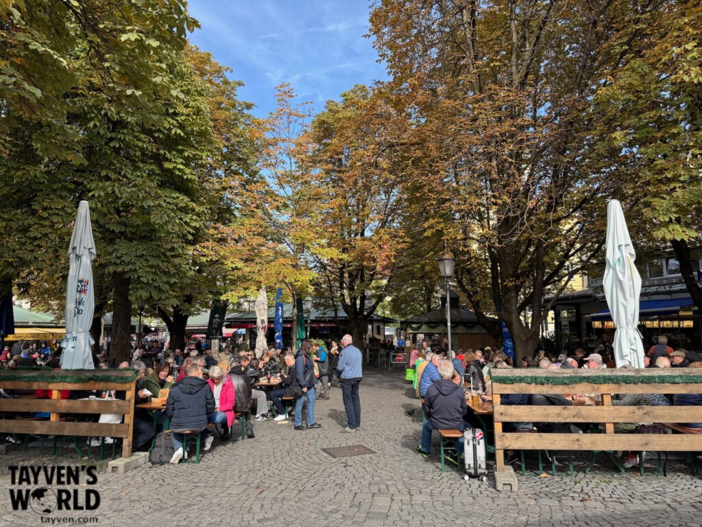 Busy outdoor beer garden and food market beneath trees at Viktualienmarkt Munich