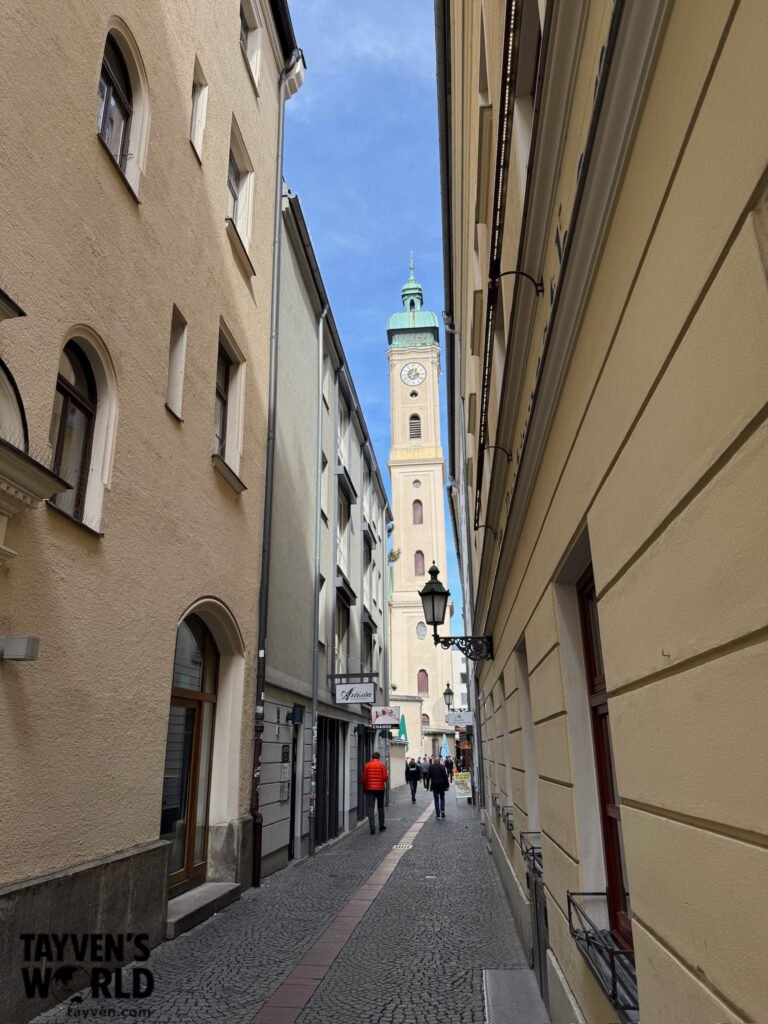 Narrow cobbled Munich Old Town lane leading toward a church clock tower