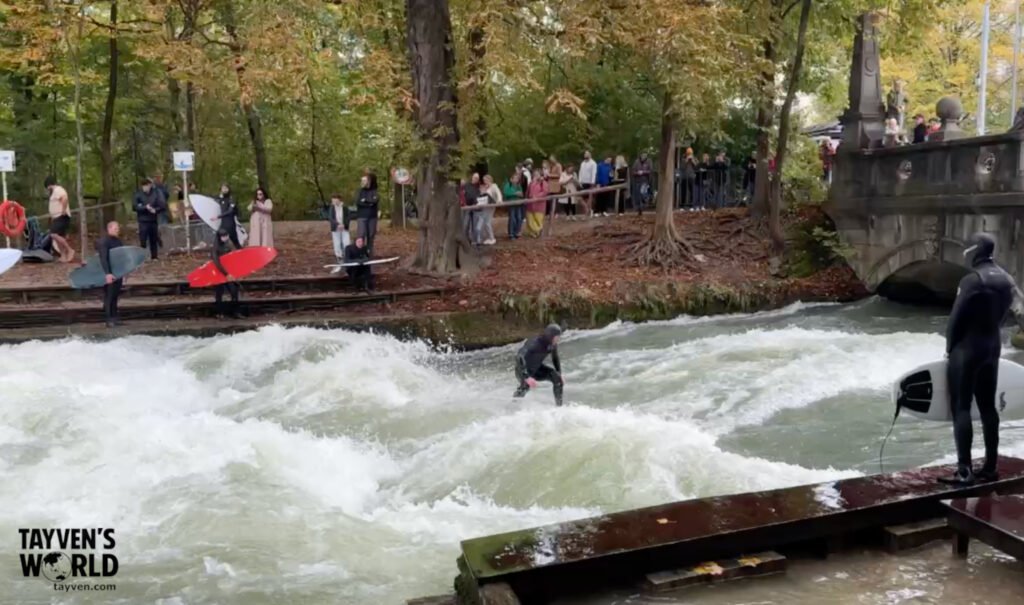 Surfer riding the Eisbach wave while others wait with boards in Munich