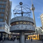 World Clock at Alexanderplatz with the Berlin TV Tower and passing trams behind it